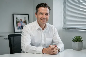 Homme en chemise blanche au bureau avec un sourire figé et une expression contrôlée illustrant le comportement d'un pervers narcissique en façade sociale